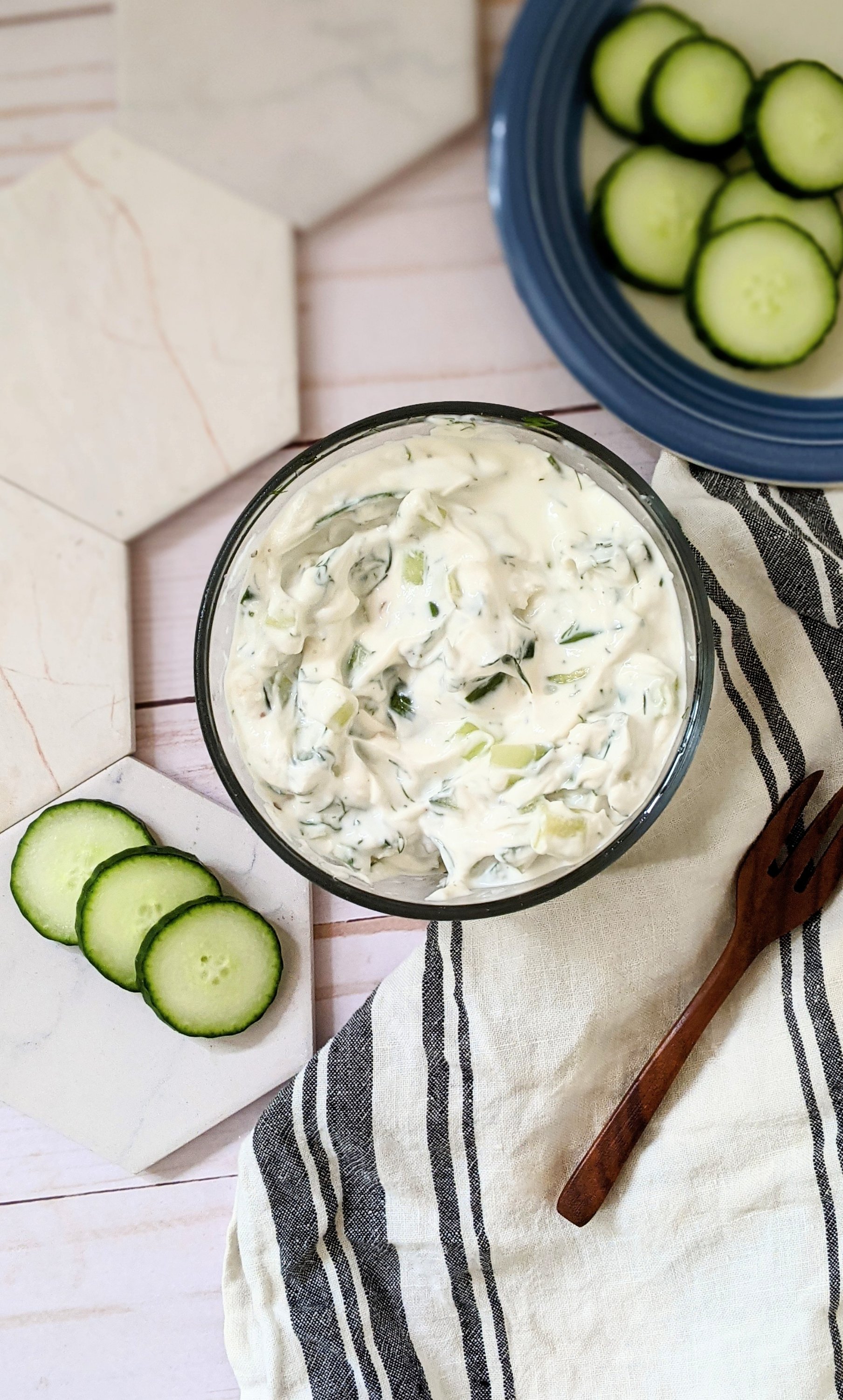 tzatziki with sour cream dill yogurt cucumbers and fresh chopped herbs on a plate with freshly sliced cucumbers and a fork.