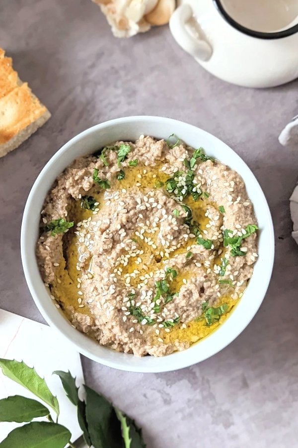 vegan eggplant dip in a bowl with tahini garlic olive oil sesame seeds paste, salt, pepper, and lemon juice with bread to dip on the side.