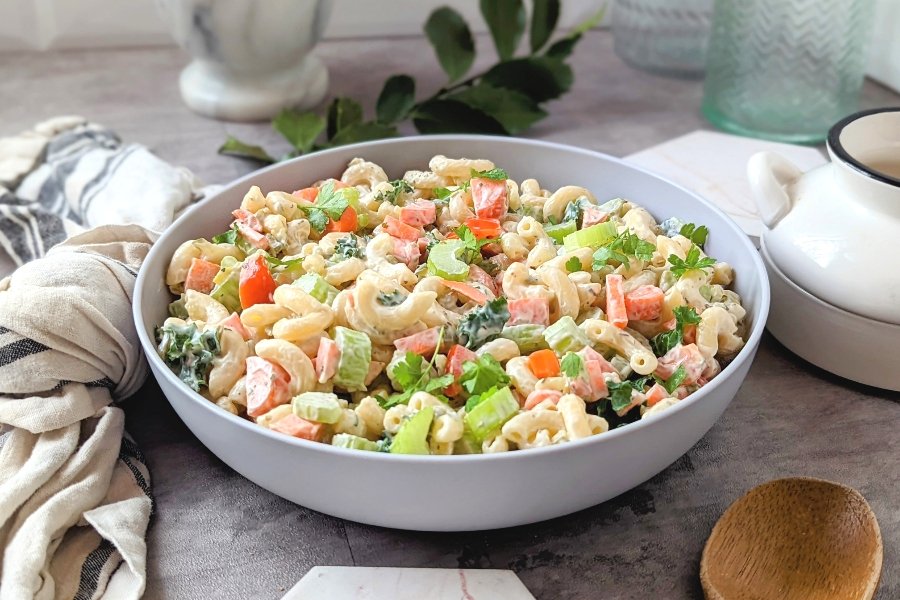 creamy ranch pasta salad with macaroni noodles in a bowl with celery chopped carrots and cherry tomatoes with a spoon.