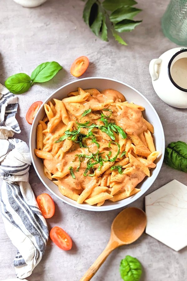 vegan vodka sauce with penne pasta in a bowl with basil leaves and cherry tomatoes with a spoon.