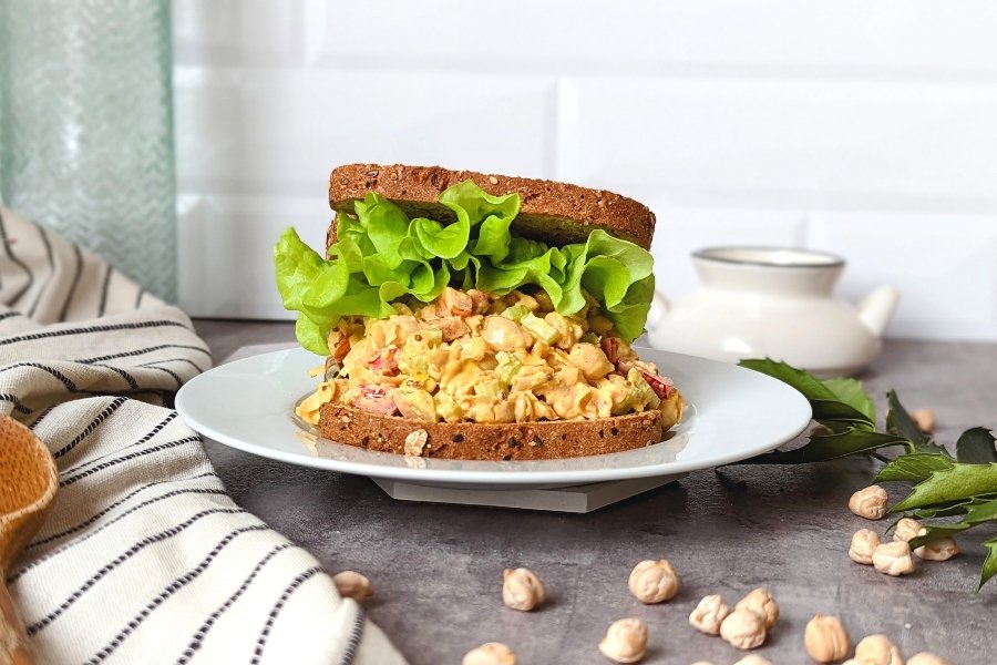 plant based chicken salad sandwich with red pepper celery and a creamy dressing on a plate with curly leaf lettuce on the sandwich.