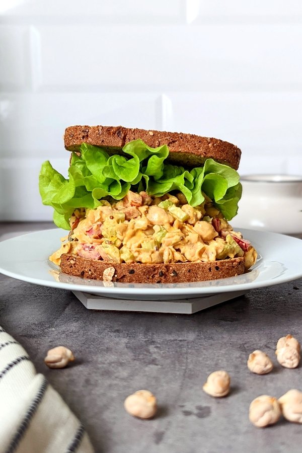 vegan chickpea salad with chickpeas recipe sandwich stacked with lettuce toppings and chickpeas with dried chickpeas on the table.