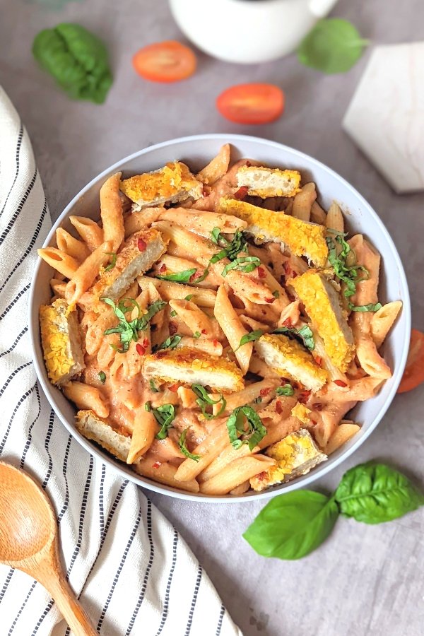 penne alla vodka with chicken recipe hearty creamy penne pasta noodles with crispy breaded chicken breast slices in a bowl with fresh basil and chopped tomatoes.