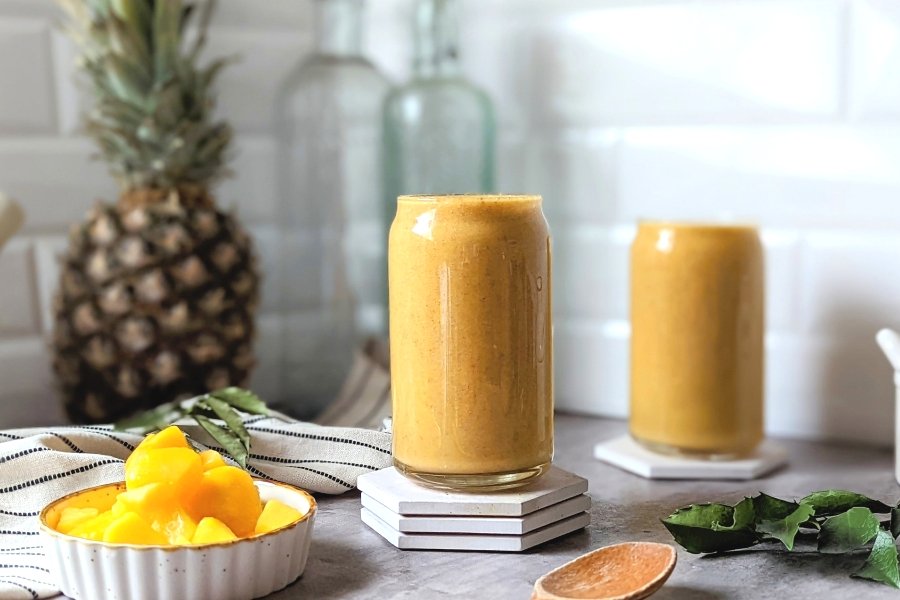 healthy pineapple mango smoothie dairy free made with protein powder flaxseeds and ginger powder healthy antioxidant breakfast in two serving glasses with fresh pineapple and mangoes.