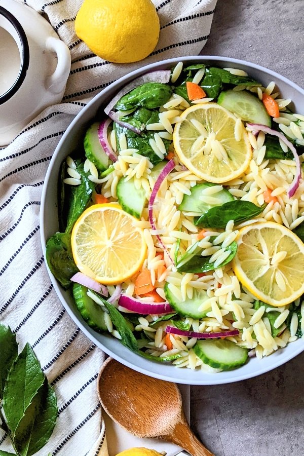 close up of a bowl of lemon orzo pasta salad with cucumber carrots dill fresh mint in a bowl.