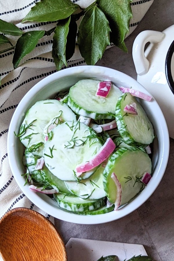 fresh cucumber mayo salad recipe with creamy dressing with mayonnaise vinegar sugar dill salt and pepper with red onions in a white dish ready for serving at a summer bbq or cookout.
