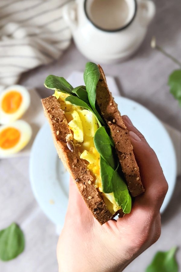 gluten free egg and mayo sandwich recipe with spinach dijon or whole grain mustard and hardboiled eggs being held over a plate.