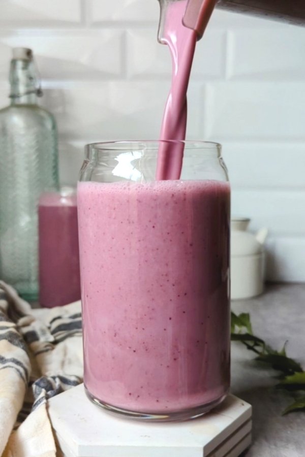 high protein yogurt smoothie with blueberries banana oats orange juice and flaxseeds being poured into a glass from a blender.