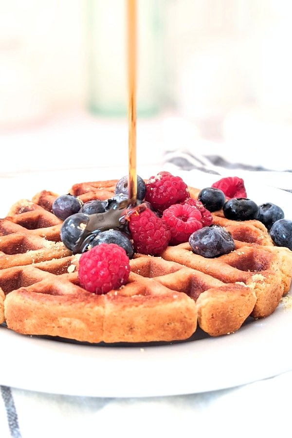 egg free waffles with maple syrup and raspberries blueberries and blackberries on a plate with fresh home tapped maple syrup.