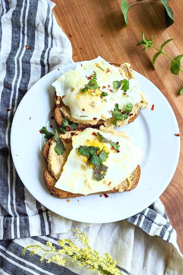 eggs and hummus recipe on toasted bread with chili flakes and a white and blue striped napkin in a modern farmhouse kitchen.