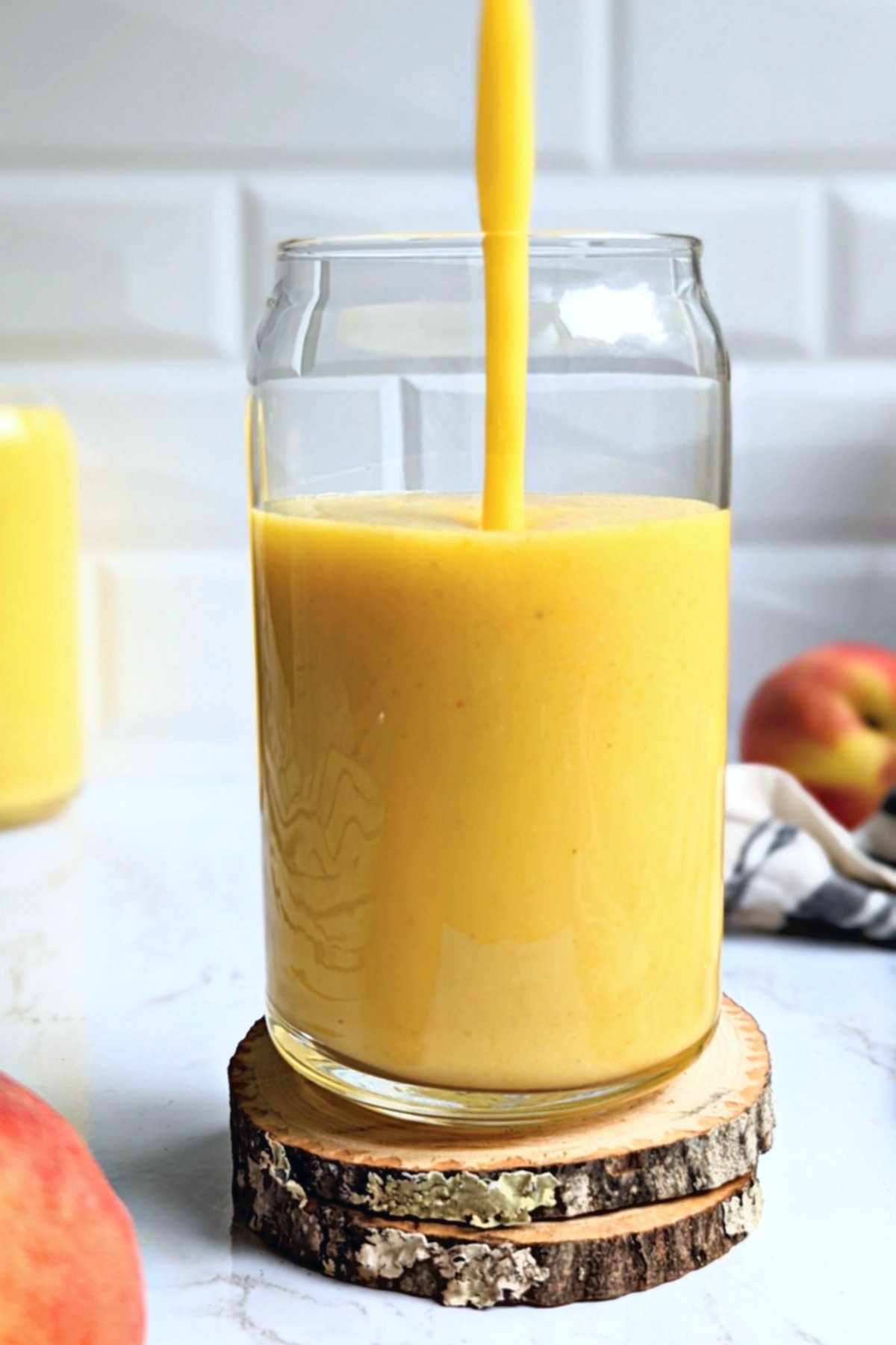 vegan gluten free peach pineapple smoothie being poured into a can shaped glass in a white kitchen with wooden coasters