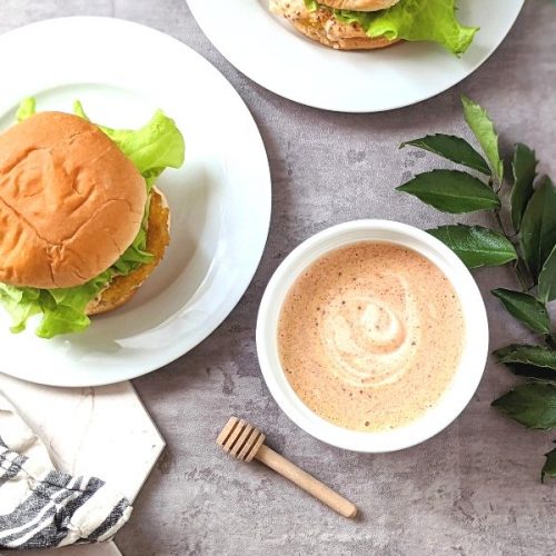 chicken sandwich sauce recipe with honey mustard mayo spices paprika and spicy chili flakes in a ramekin drizzled on a chicken sandwich with a honey dipper.