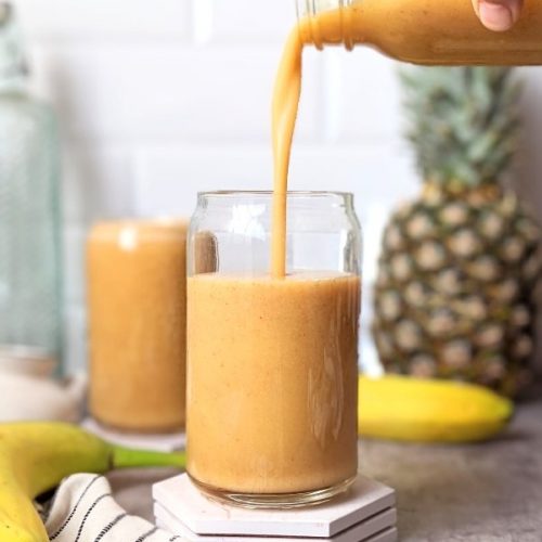 pineapple banana smoothie recipe poured into a can glass with fresh bananas and a pineapple in the background.