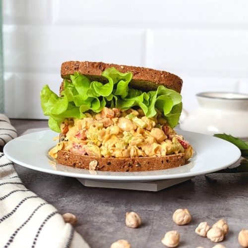 plant based egg salad sandwich with red pepper celery and a creamy dressing on a plate with curly leaf lettuce on the sandwich.