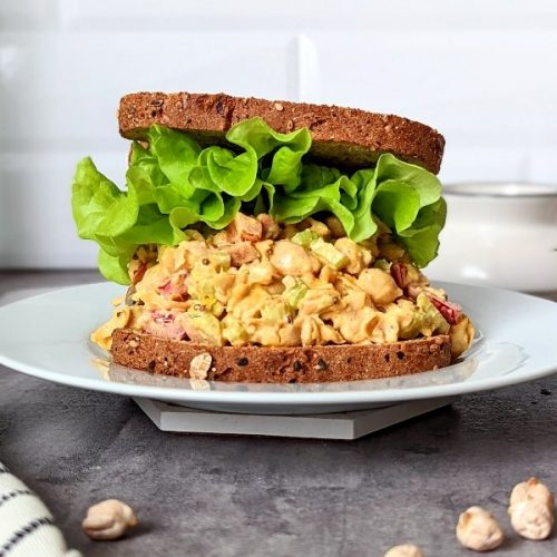 vegan chicken salad with chickpeas recipe sandwich stacked with lettuce toppings and chickpeas with dried chickpeas on the table.