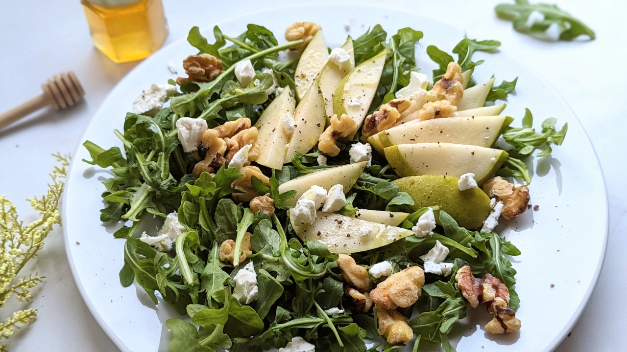 arugula salad recipe with pears and honey dijon vinaigrette dressing with walnuts on a plate. a fancy salad recipe.
