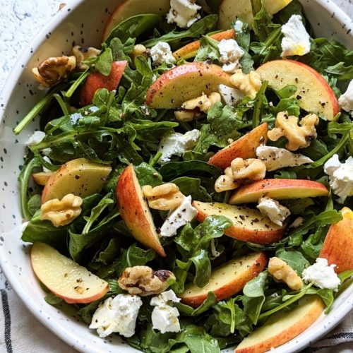apple rocket salad recipe with arugula goat cheese honey and walnuts in a bowl with sliced apples.
