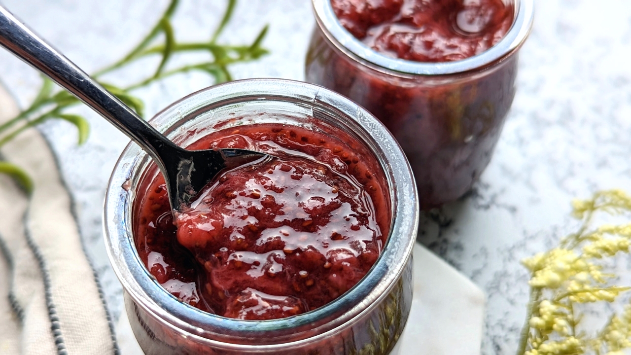 easy homemade frozen strawberry jam recipe bring scooped out by a spoon from a small cute glass jar, easy homemade jam recipe with lemon and chia seeds.