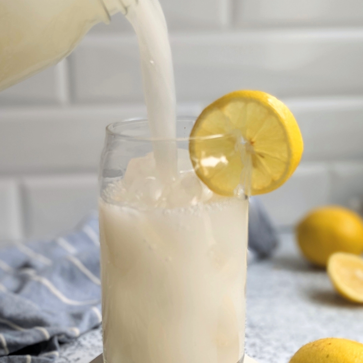 coconut lemonade being poured into a fancy mason jar can glass with a slice of lemon in a modern kitchen