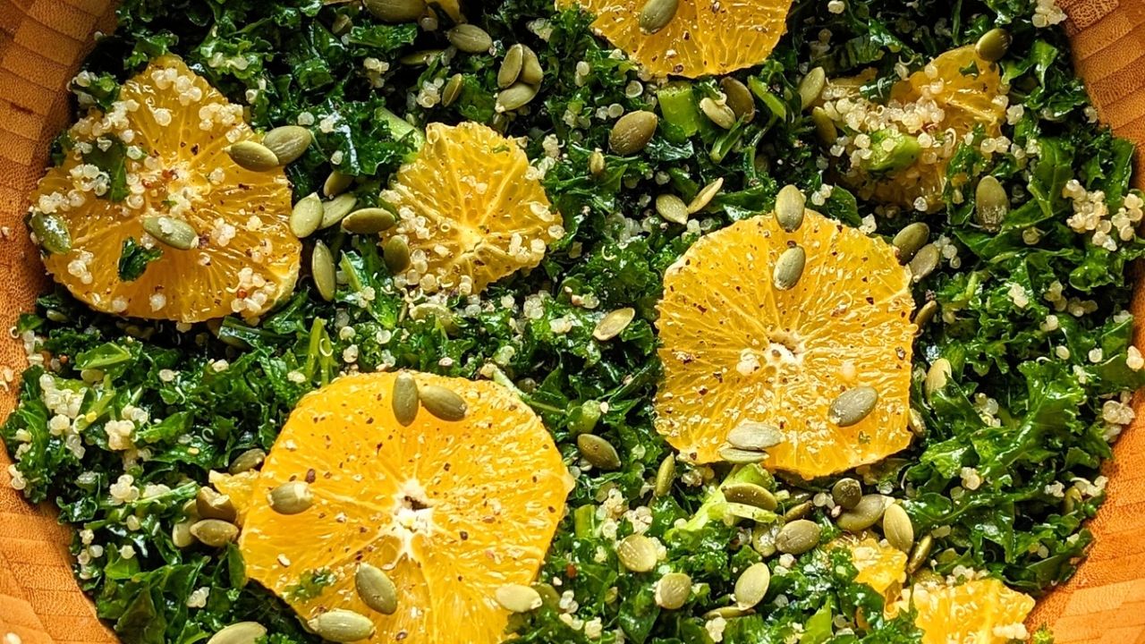 orange kale salad recipe with quinoa and balsamic vinegar in a large wooden serving bowl with pepitas pumpkin seeds