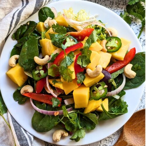 Thai mango salad with cashews ripe mangoes red onion bell pepper and a tangy lime dressing over mixed greens on a white plate