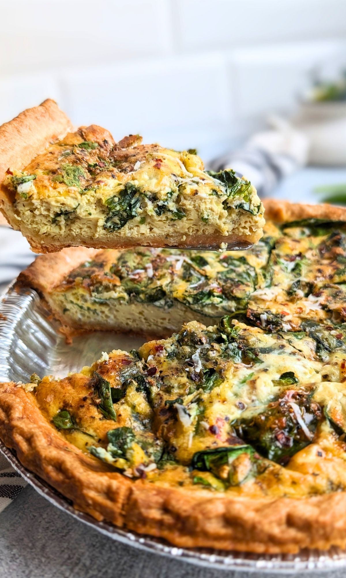 a slice of quiche florentine with spinach and parmesan cheese and red pepper flakes with a store bought crust