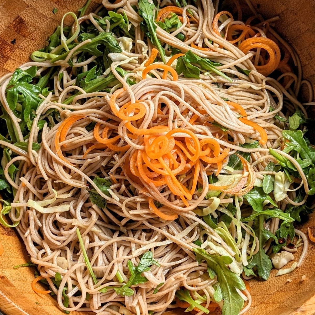 a large wooden bowl full of spicy soba noodle salad with veggies and a tangy homemade lime dressing