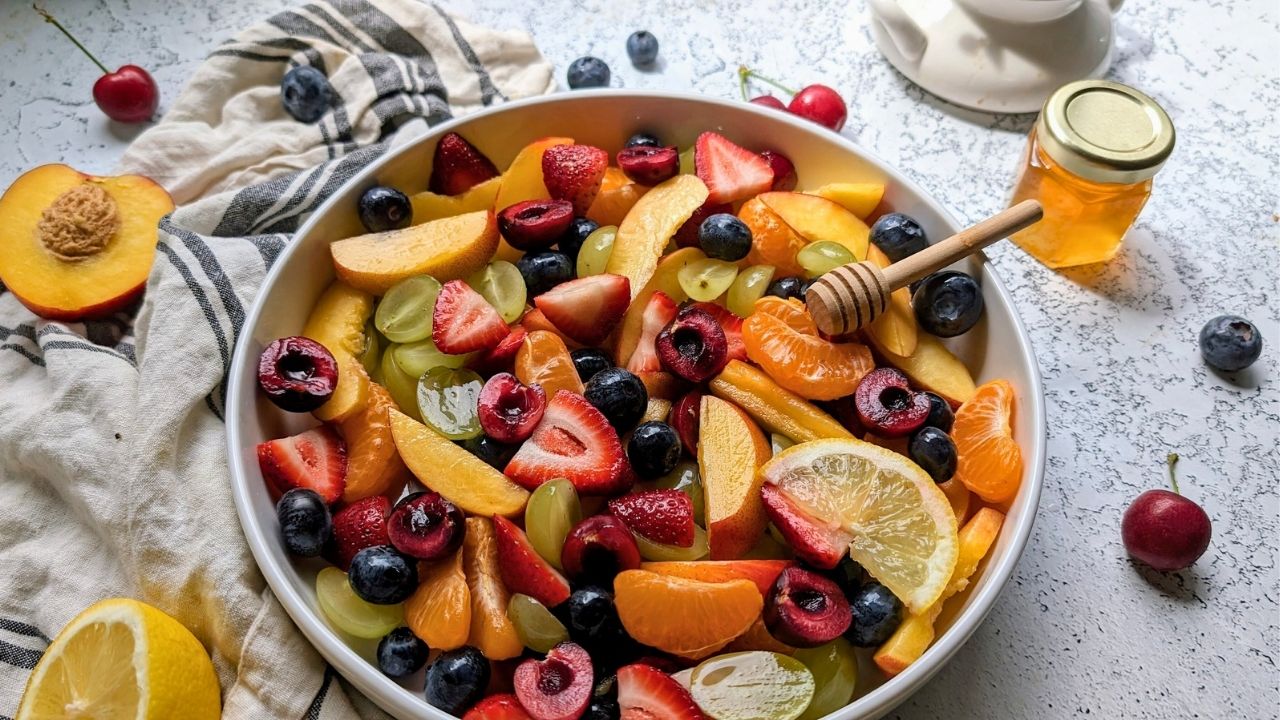 honey and lemon fruit salad with stone fruits, grapes, oranges, and berries with a honey dipper in the bowl