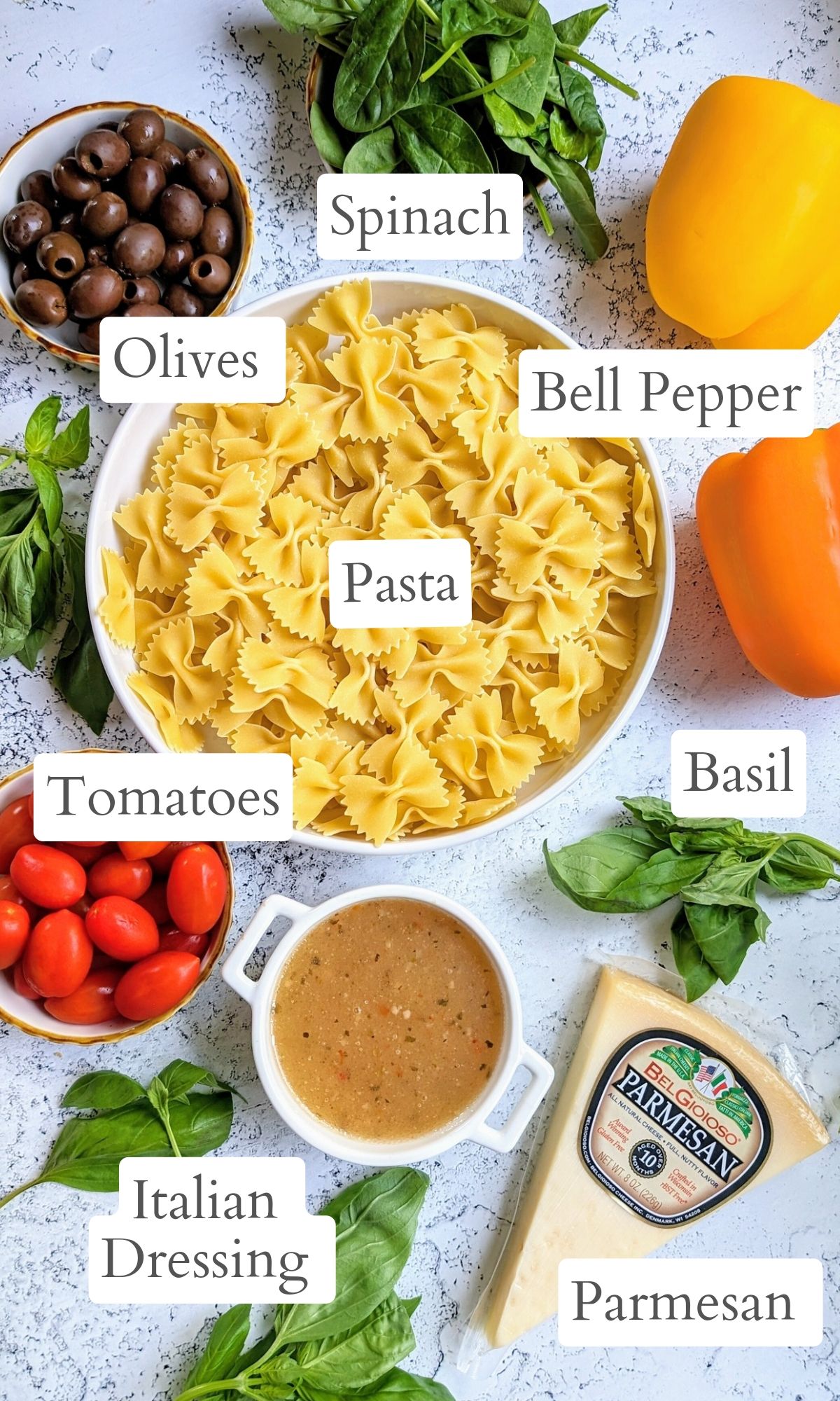 italian bowtie pasta salad ingredients like dried noodles, tomatoes, bell pepper, fresh basil, black olives, italian dressing, and parmesan cheese.