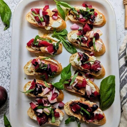 a psummer appetizer plate of plum and ricotta bruschetta for guests topped with fresh basil and olive oil