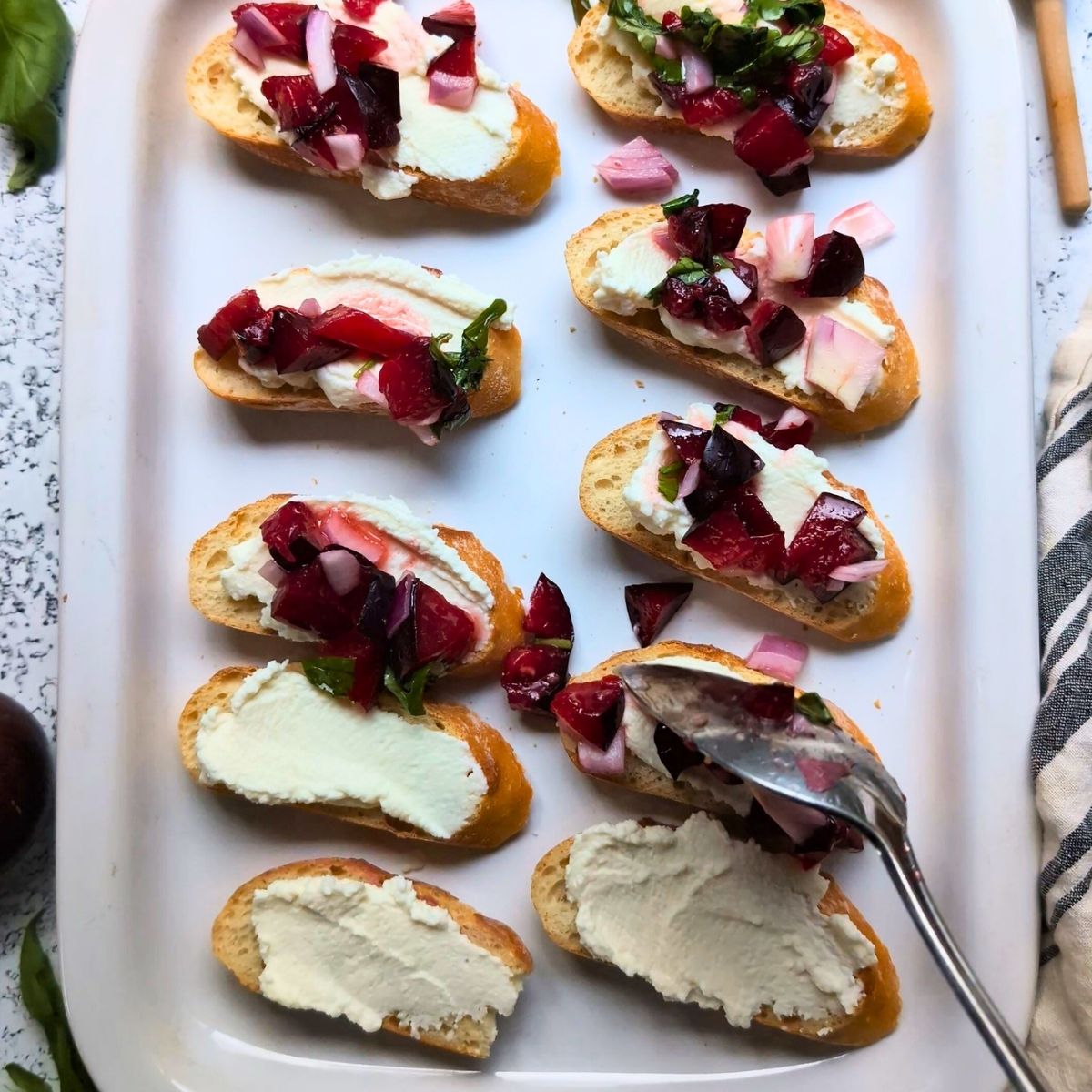 ricotta toasts being topped with a spoonful of chopped plum bruschetta