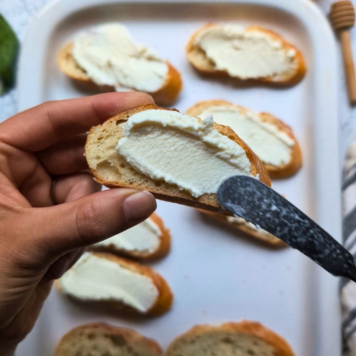 a cheese knife spreading ricotta cheese on a toasted baguette.