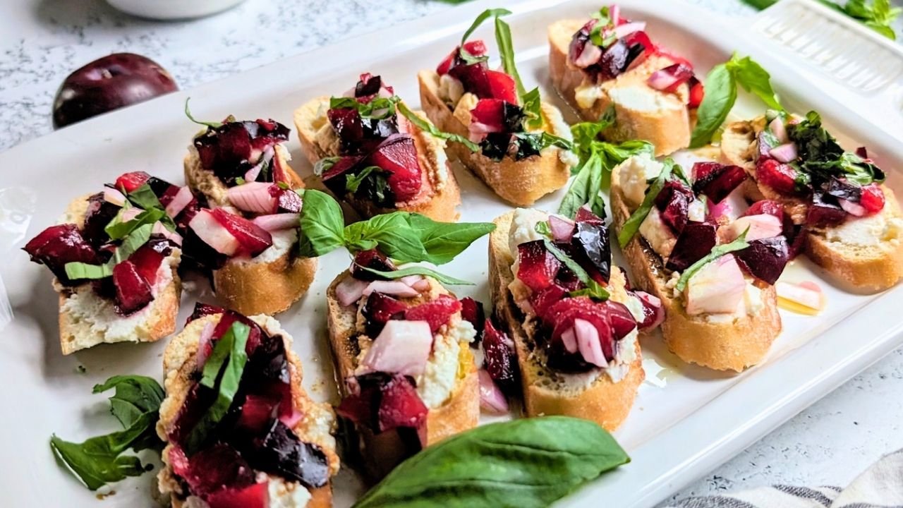 a tray of toasted baguette slices with creamy ricotta cheese and a bright and sweet plum bruschetta topping with fresh basil.