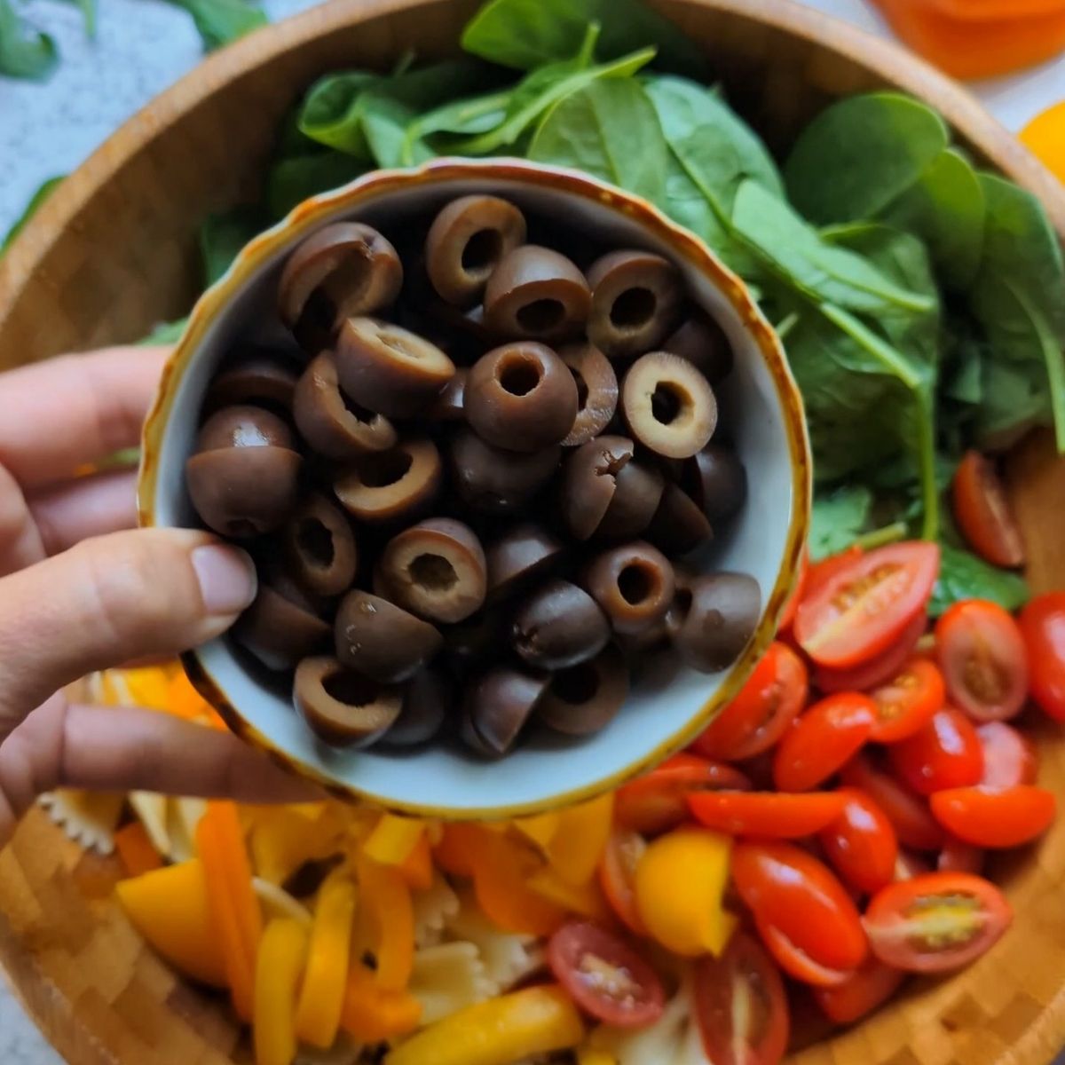 a large bowl full of black olives cooked bowtie pasta, spinach, and bell peppers.