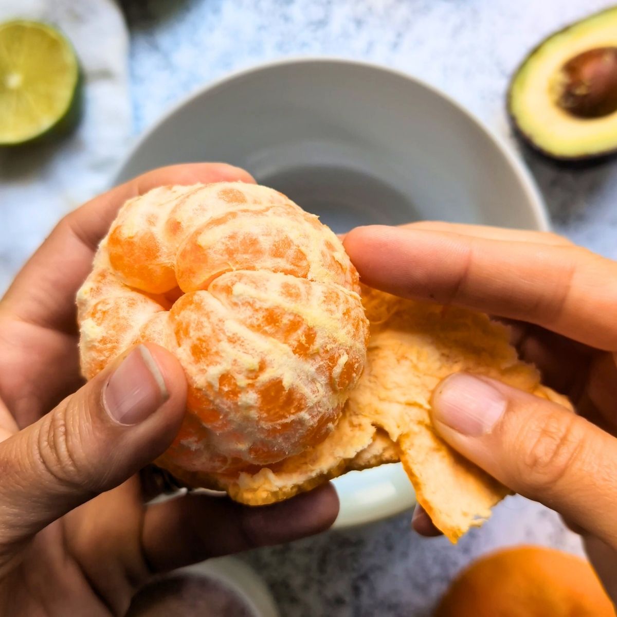 hands peeling an orange and adding the segments to a bowl.
