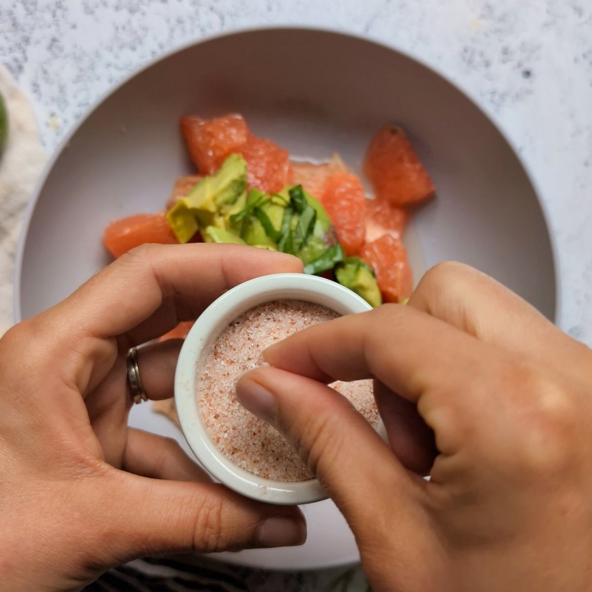 hands adding a pinch of salt over the grapefruit and avocado salad in a bowl.