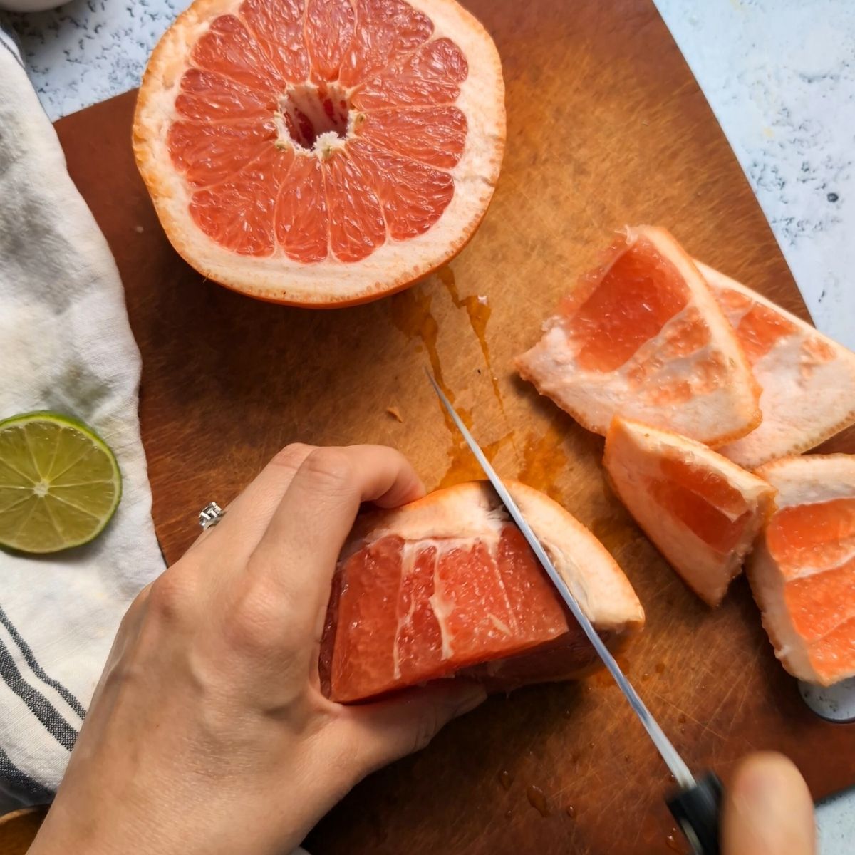 a knife cutting away the skin of the grapefruit carefully on a cutting board.