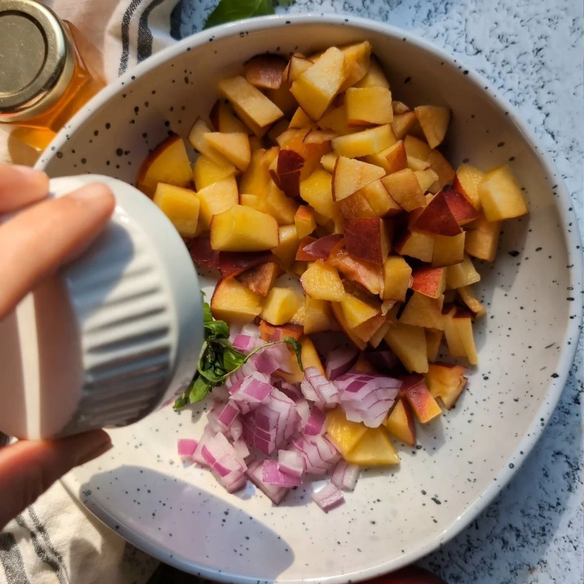 a bowl of chopped peaches, chopped red onion, and fresh basil, with garlic.