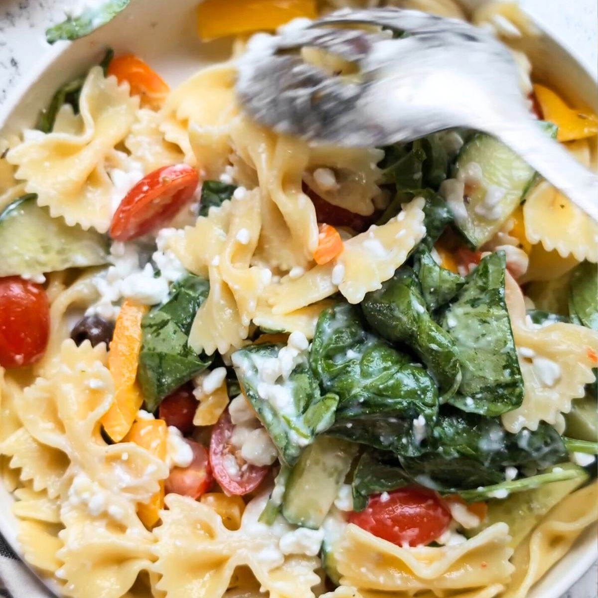 a metal spoon stirring cottage cheese into the pasta and veggie salad recipe.