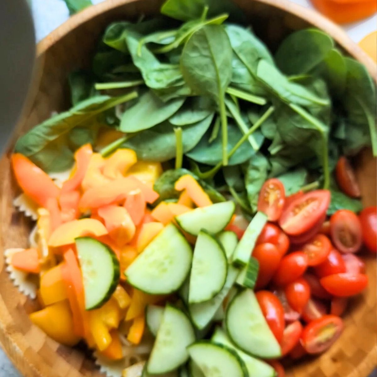 a large bowl with pasta, cucumbers, tomatoes, spinach, and bell peppers for a vegetarian pasta salad.