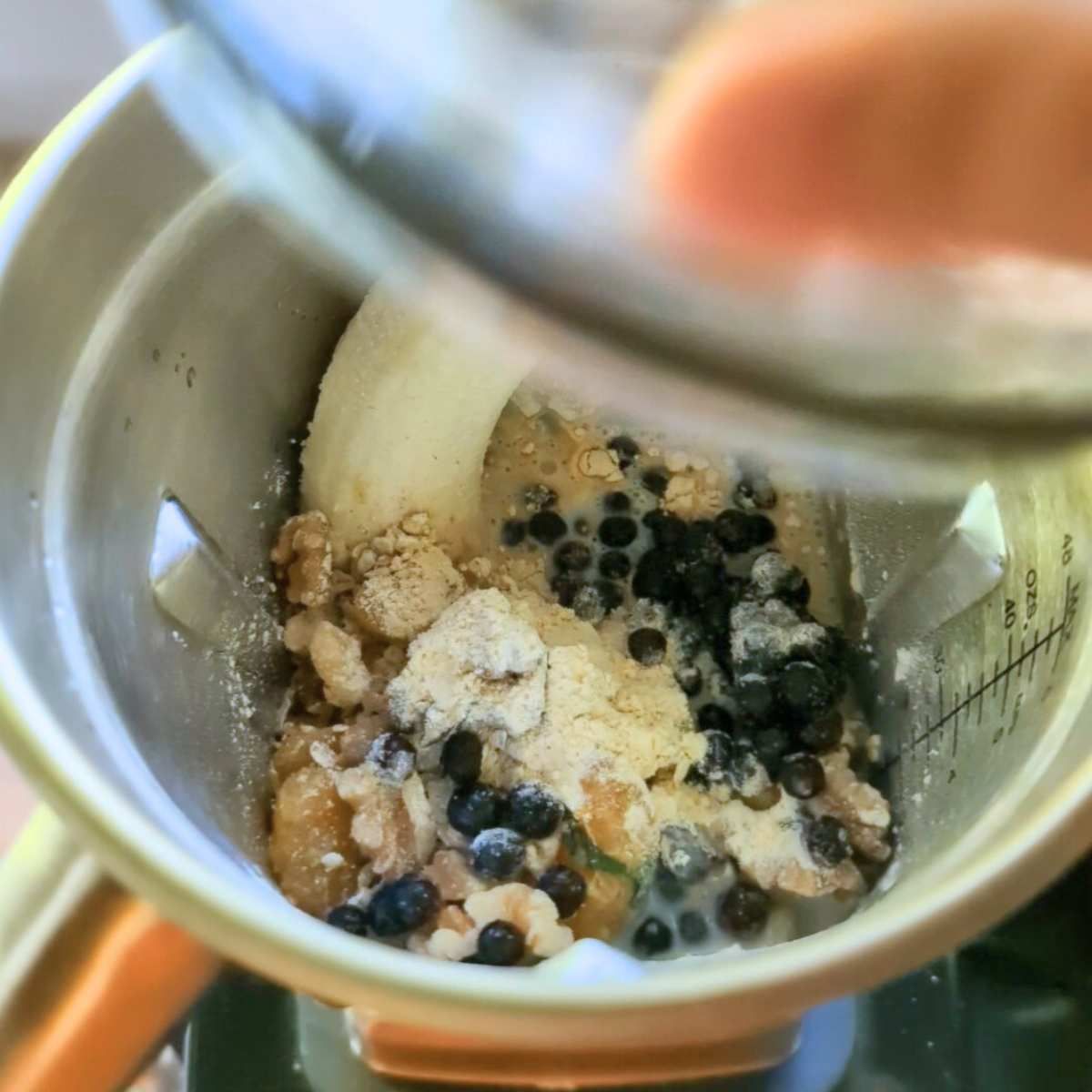 a hand putting a lid on a blender full of banana, oatmeal, blueberries, walnuts, and protein powder.