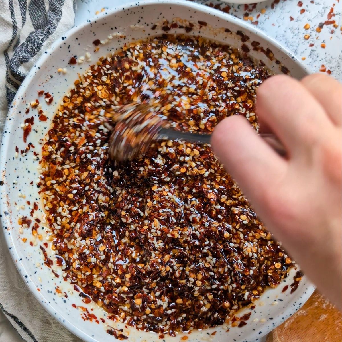 a hand stirring and mixing homemade chili crisp condiment with honey and red pepper flakes.