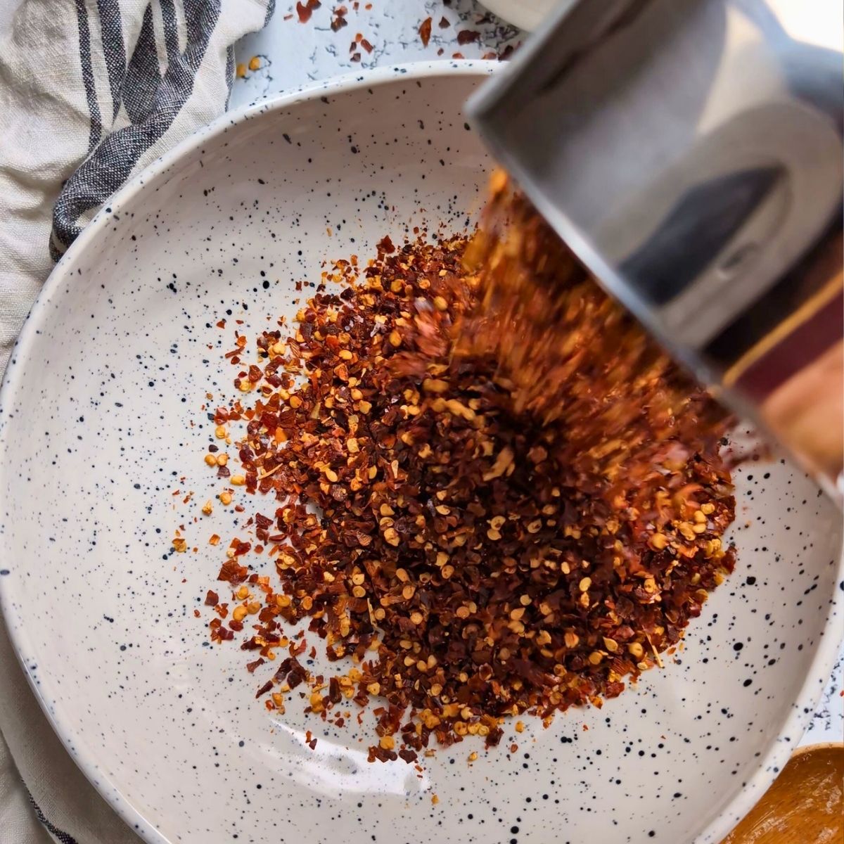 a measuring cup pouring crushed red pepper chili flakes into a large bowl.