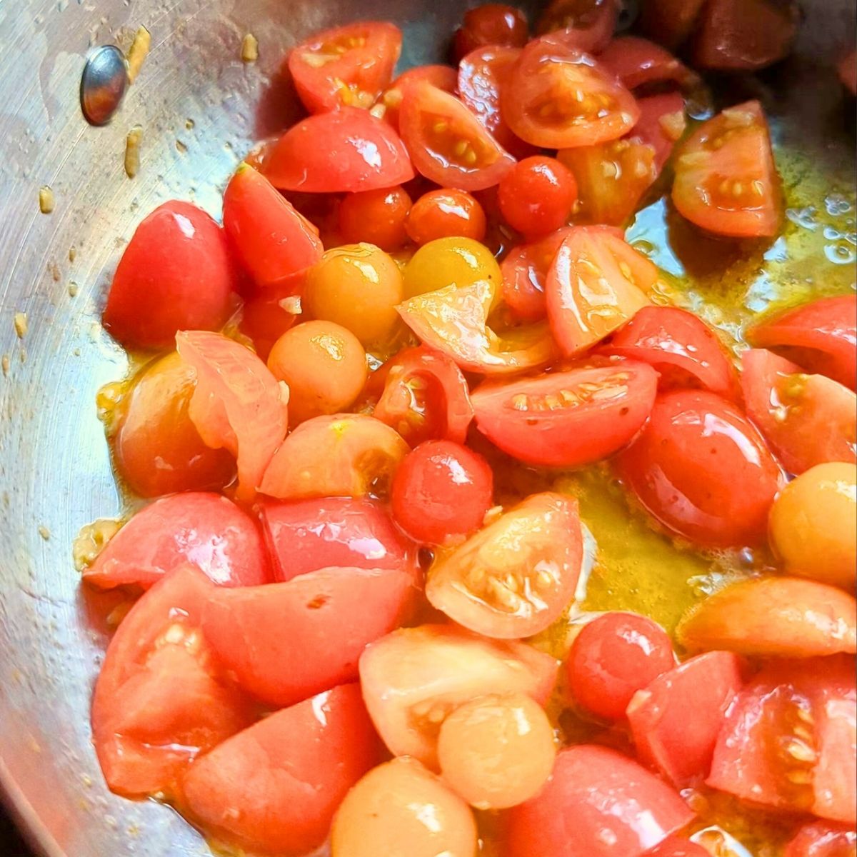 fresh cherry tomatoes being added to a pan with garlic and olive oil.