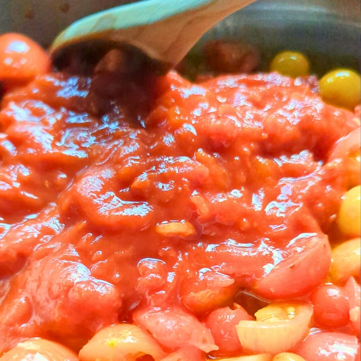 canned san marzano and fresh cherry tomatoes in a pan being stirred into garlic and olive oil.