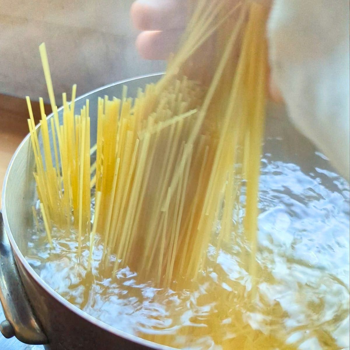 angel hair pasta being tossed into a pot of boiling water to cook.