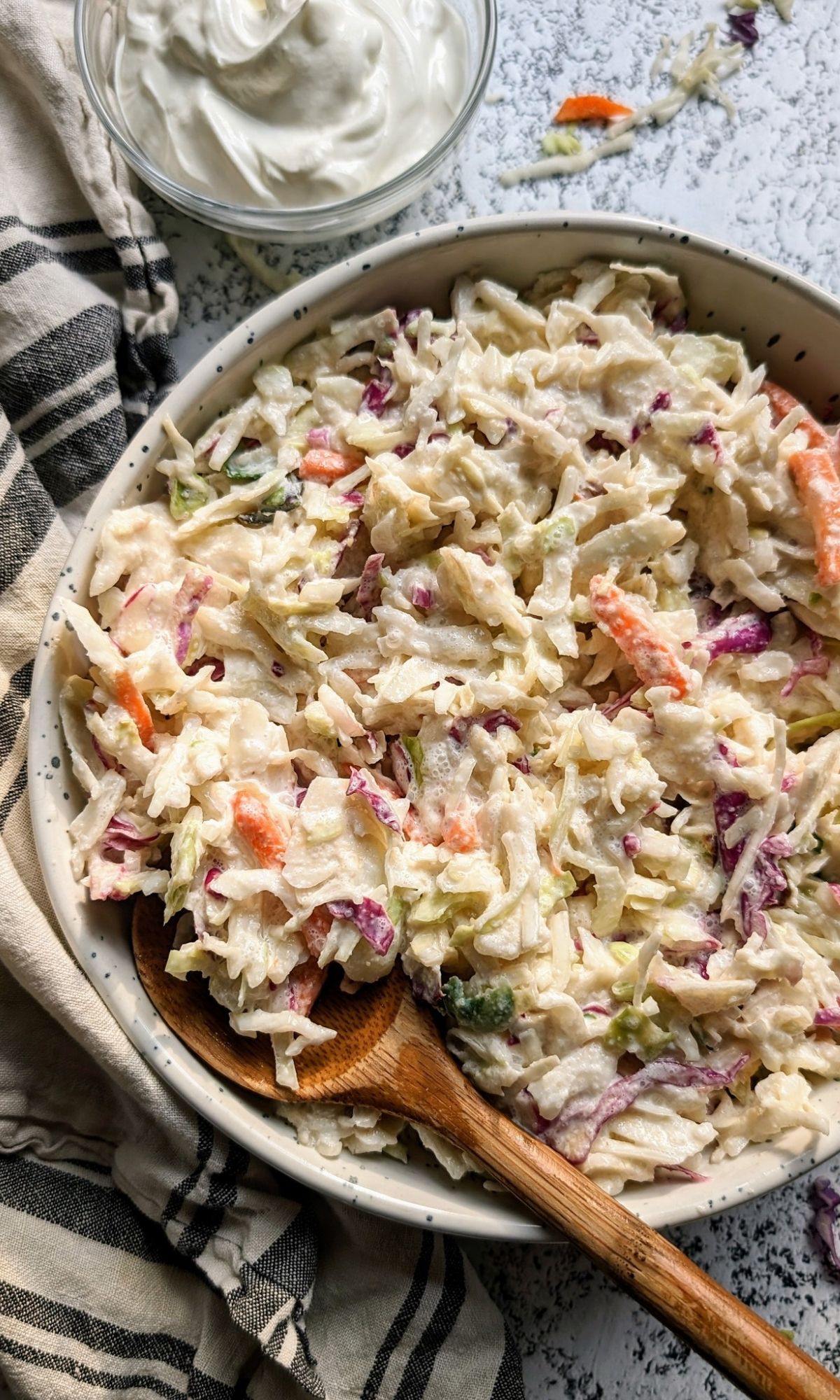 a large bowl of coleslaw with sour cream with a wooden spoon perfect for a summer bbq.