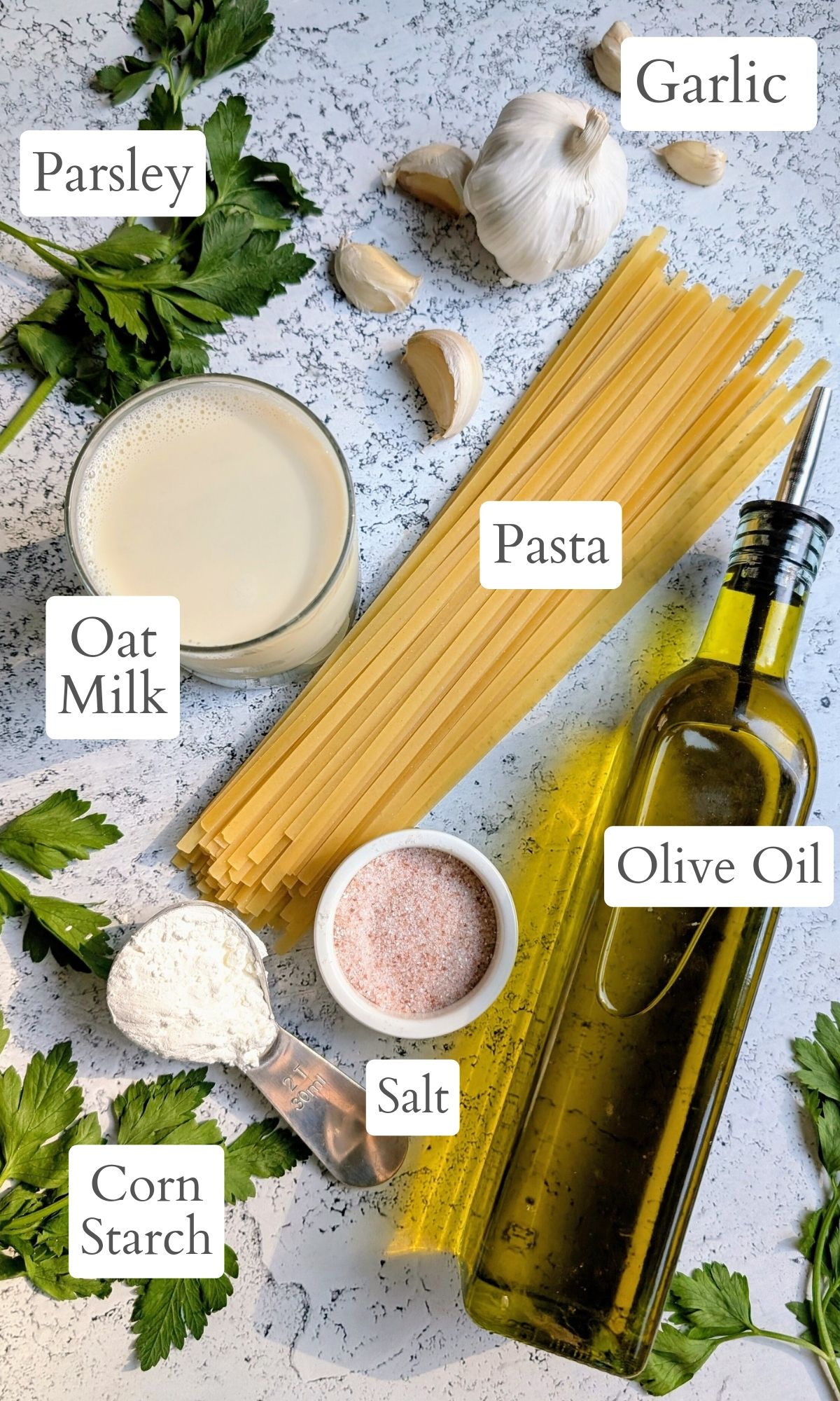 ingredients for oat milk alfredo like fettuccine pasta, olive oil, oat milk, salt, garlic, fresh parsley, and corn starch to thicken the sauce.