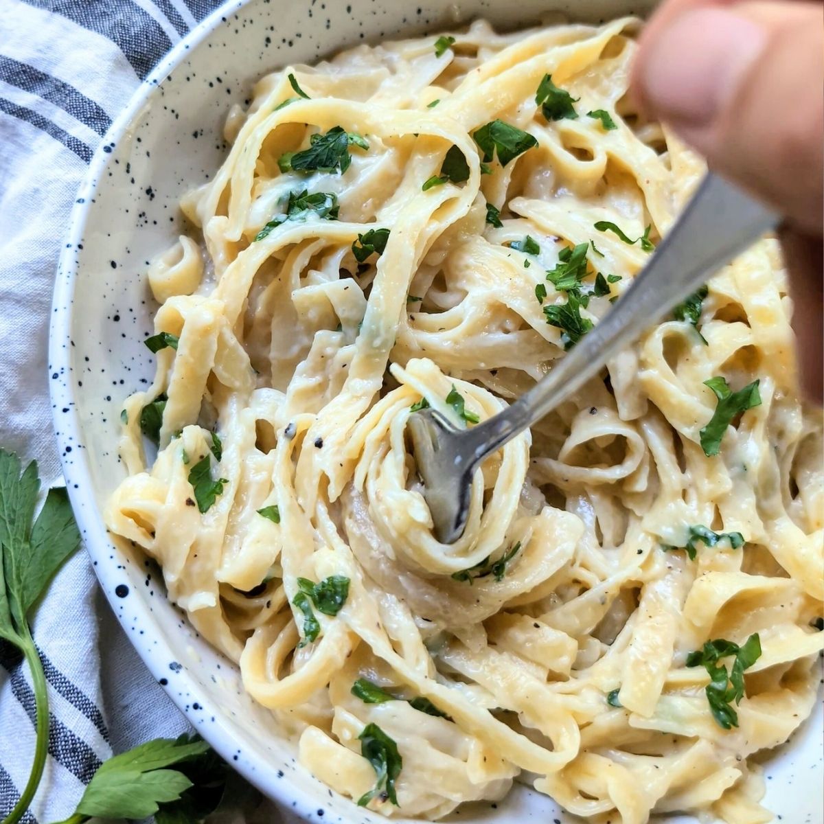 a fork twirling fettuccine pasta drenched in an oat milk alfredo sauce with fresh parsley.