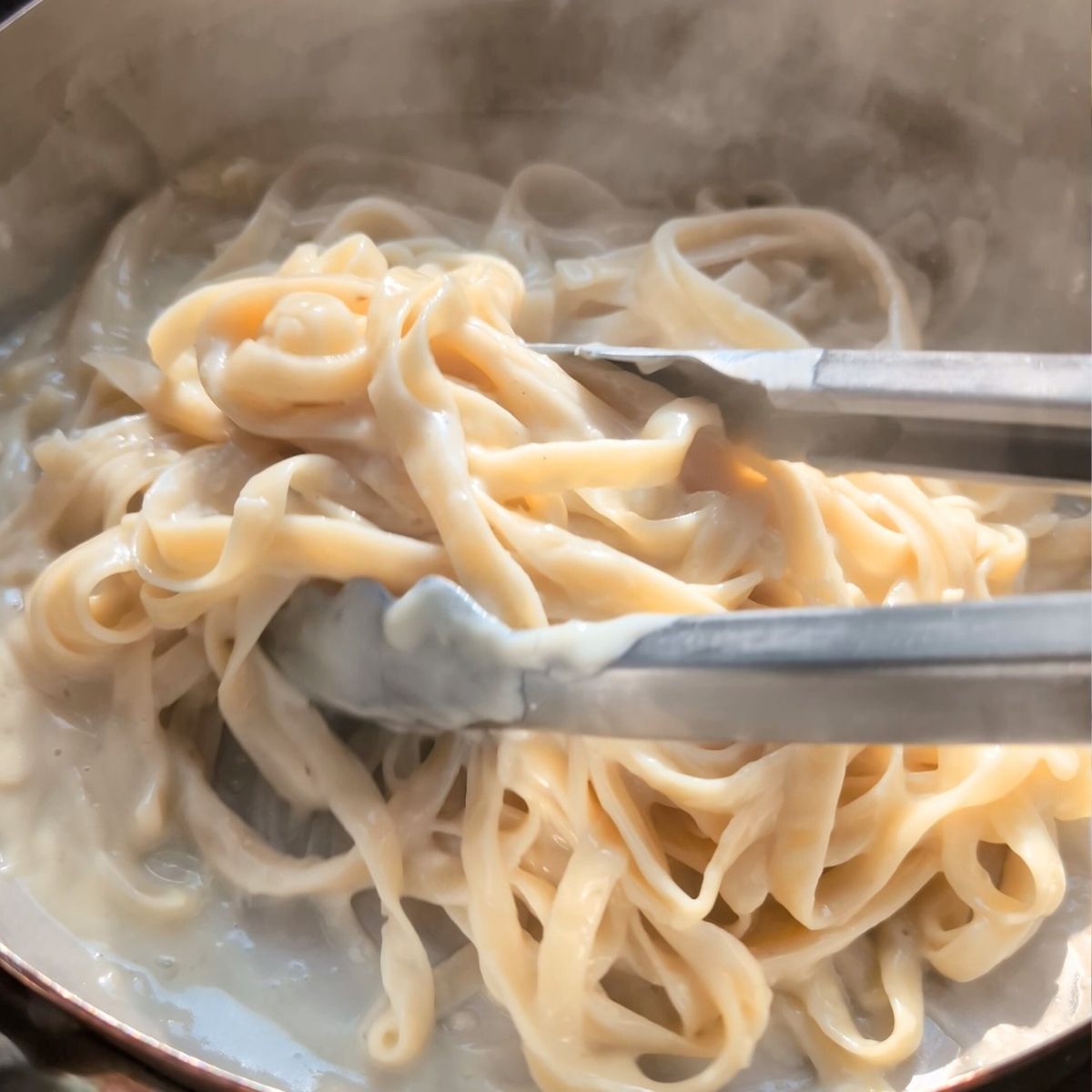 tongs tossing fresh fettuccine pasta with a creamy vegan oat milk sauce for a plant based vegan alfredo with oat milk.